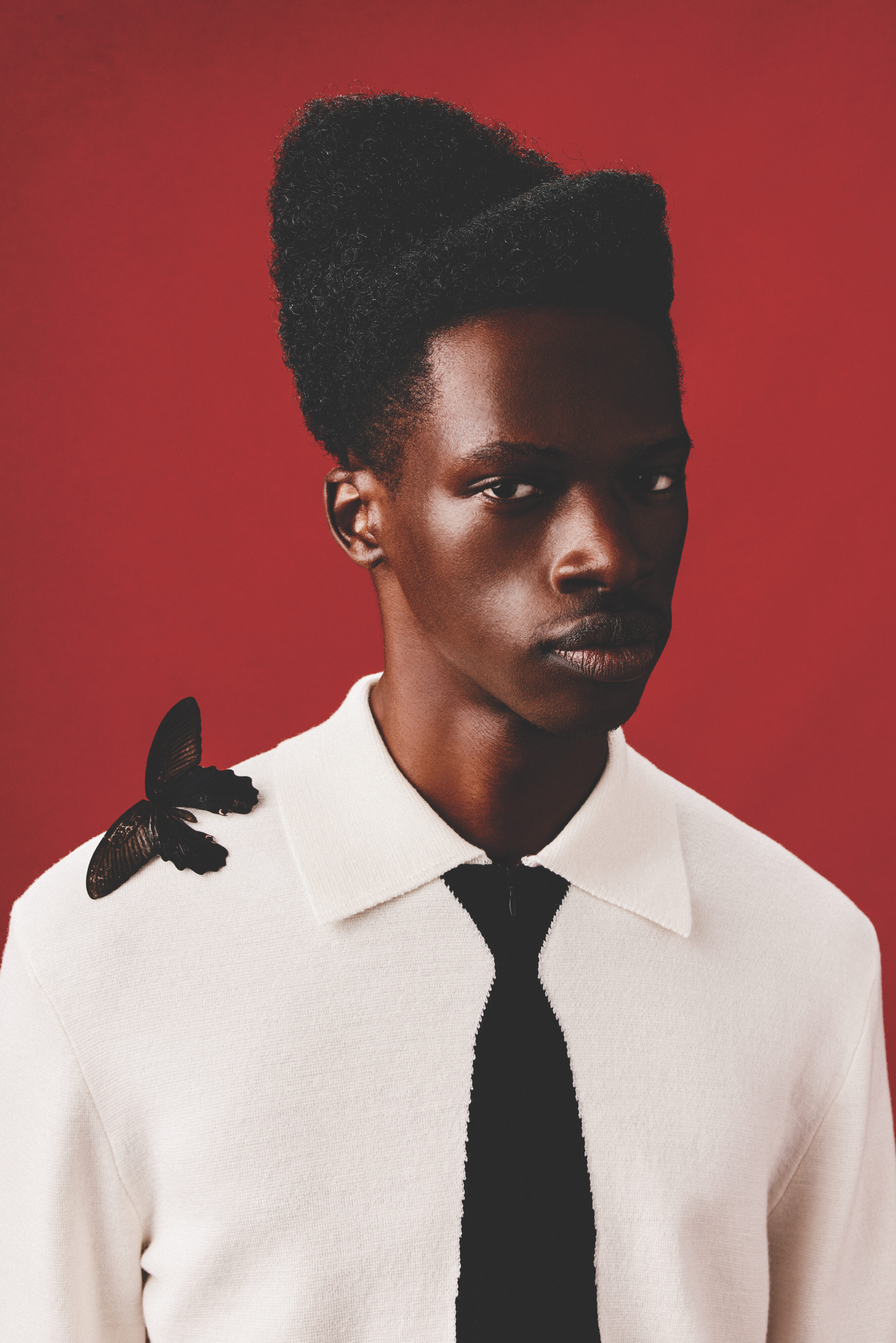 Man in white shirt and black tie against a red background with butterfly on his shoulder.