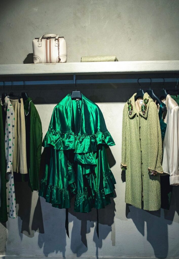 Shiny satin green dress hanging on a clothing rack next to other vintage fashion pieces. 
