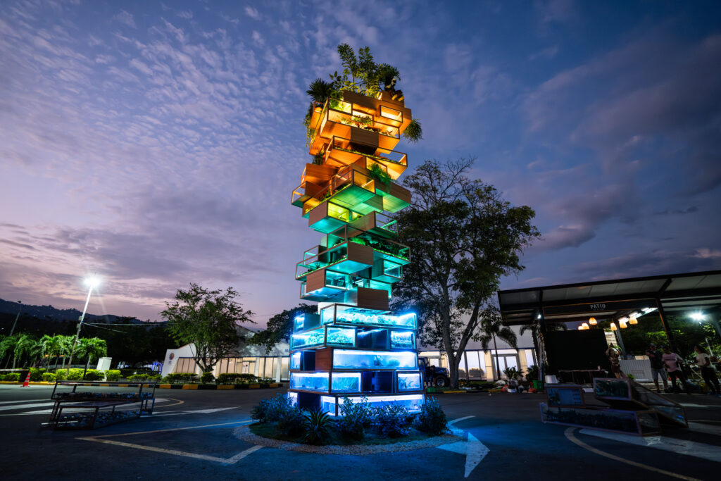 Biodiversity Jenga installation by Benjamin Von Wong illuminated at dusk, featuring stacked transparent blocks with greenery and aquatic life, highlighting environmental themes at the U.N. Biodiversity Conference.