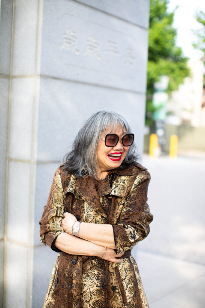 Stylish senior woman laughing in a snake-print coat and oversized sunglasses, embodying the Grandmacore fashion trend.
