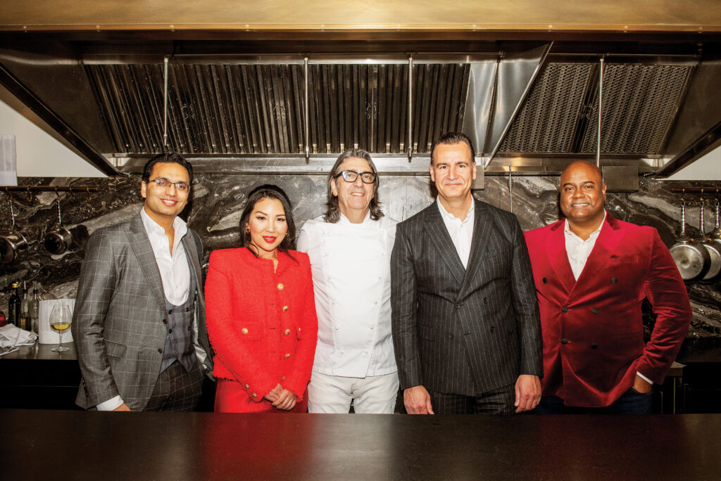 Five diverse ambassadors in elegant attire standing in a Michelin-starred restaurant kitchen, showcasing culinary excellence and cultural connections for the 3 magazine Ambassador Program launch event.