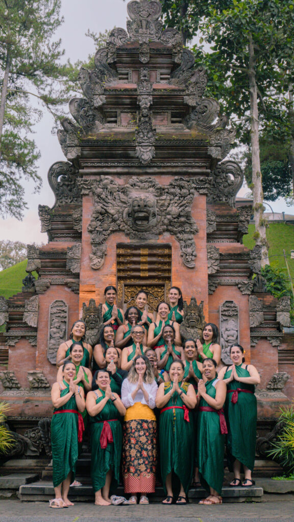 Group of women in traditional Balinese attire posing with hands in prayer at a cultural site, symbolizing empowerment and community in travel experiences for women, particularly women of color, as promoted by The Girls Trip.