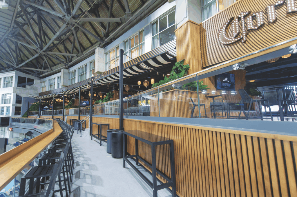 Luxury sports venue interior featuring modern seating, wooden accents, ambient lighting, and a rooftop bar atmosphere.