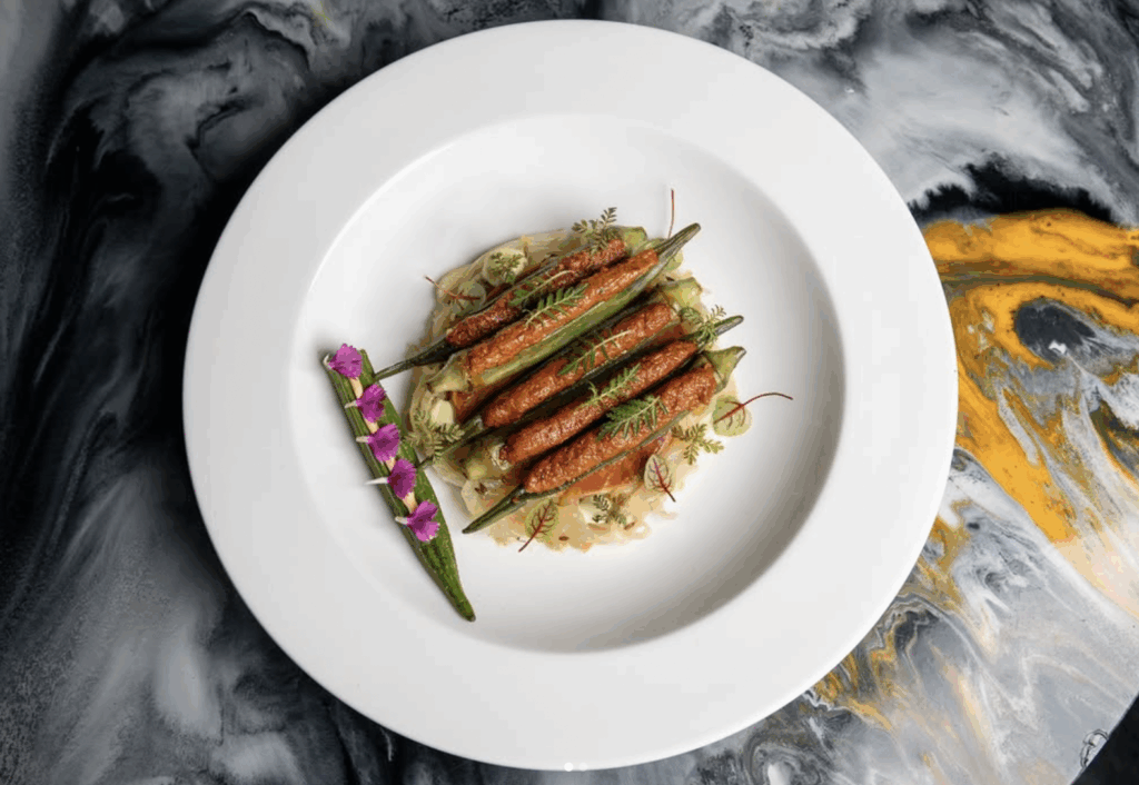 Plate featuring elegantly arranged South Asian-inspired dish with spiced carrots, okra, and garnishes, highlighting fine dining culinary artistry.