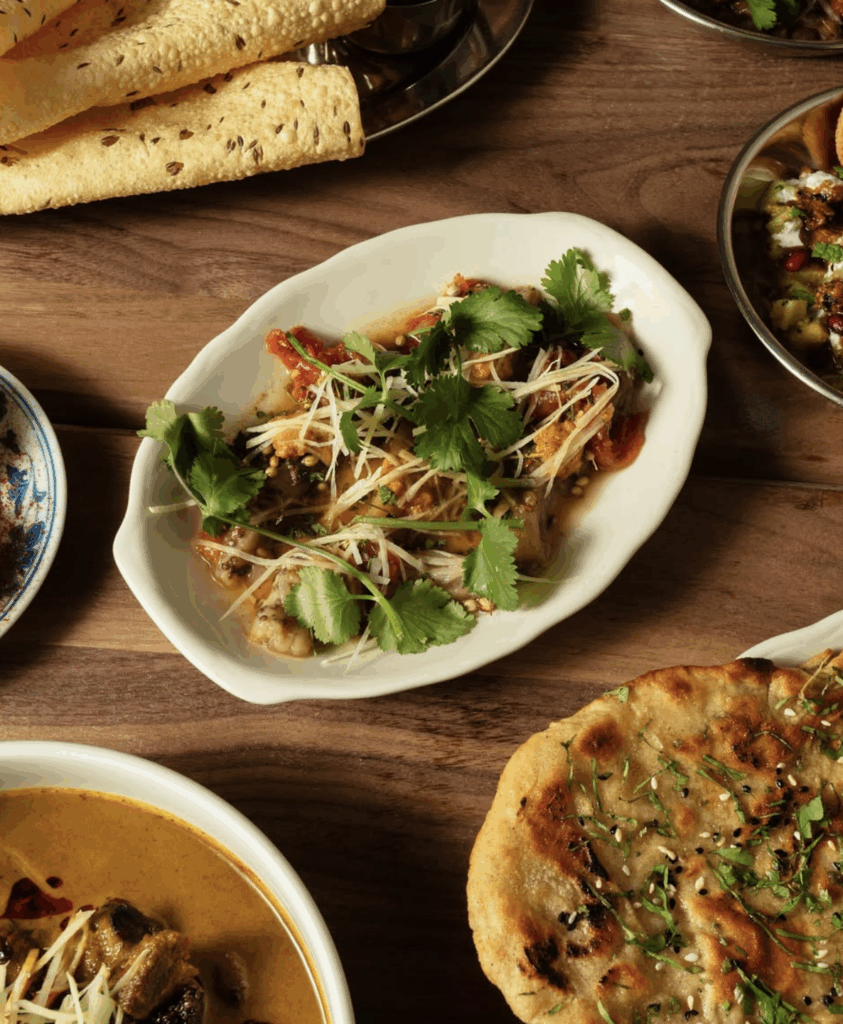 South Asian fine dining spread featuring a dish with cilantro and ginger, accompanied by crispy papad and naan, highlighting traditional culinary elements.