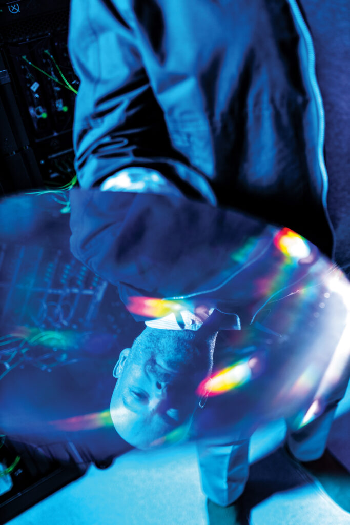 Person holding a reflective quantum computing device, surrounded by colorful light reflections, in a high-tech environment related to Xanadu's photonic quantum technology advancements.