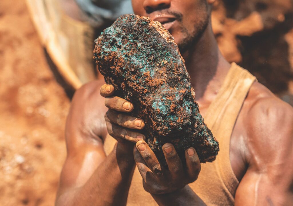 Man holding a large mineral rock with copper hues, symbolizing resource extraction in emerging energy markets like Guyana.